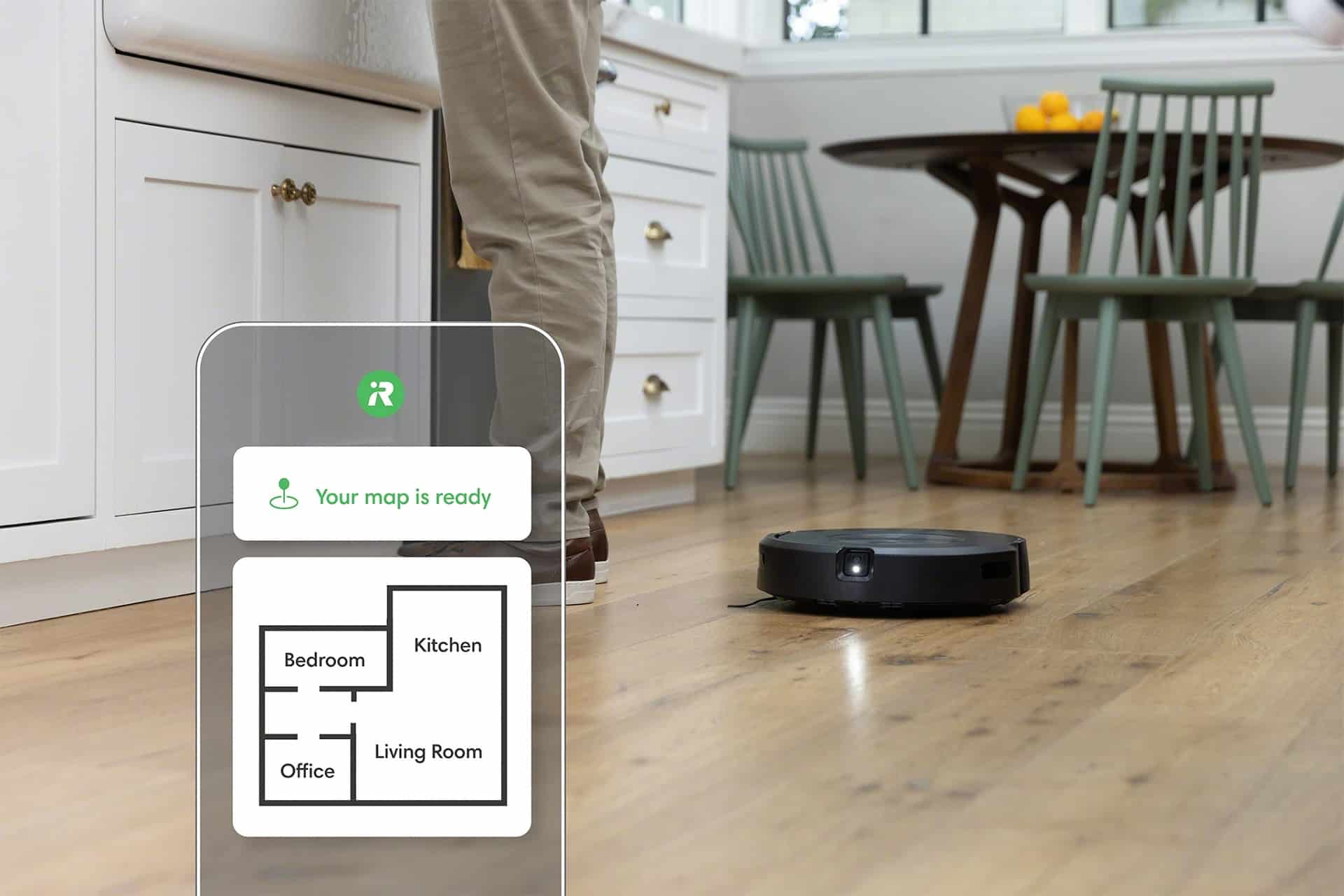 Roomba j5+ cleaning a kitchen, with an overlay of a smart phone with a home map on it.