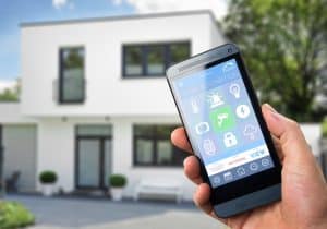 Picture of a person holding a cell phone with home automation icons in front of a house.