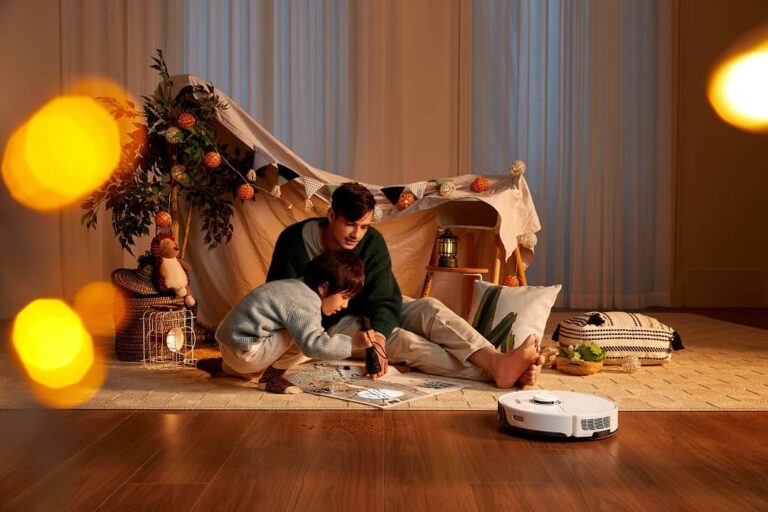 Man and child playing indoors in a make believe camping setup, Roborock vacuum cleaningi n foreground.