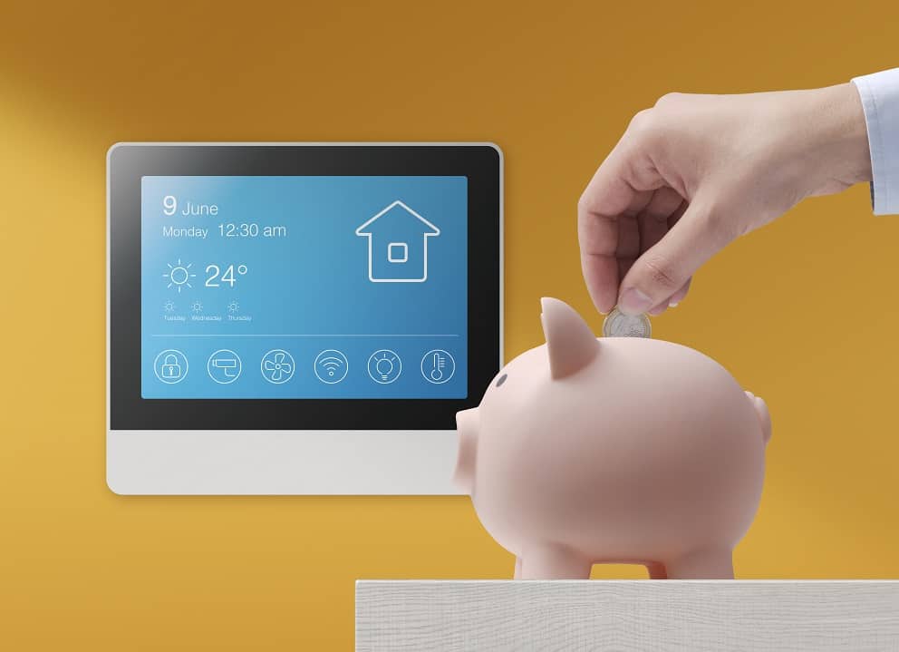 Person putting money in a piggy bank in front of a smart home control panel displayed on a tablet.