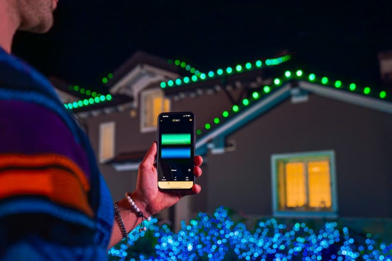 Person holding a smartphone in front of a home with Twinkly C9 lights.