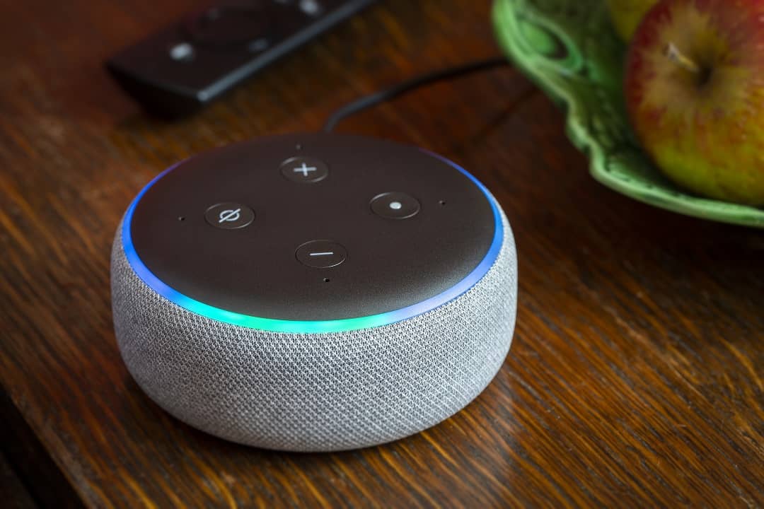 Close up of a 3rd generation Amazon Echo Dot glowing blue on a table in a domestic environment