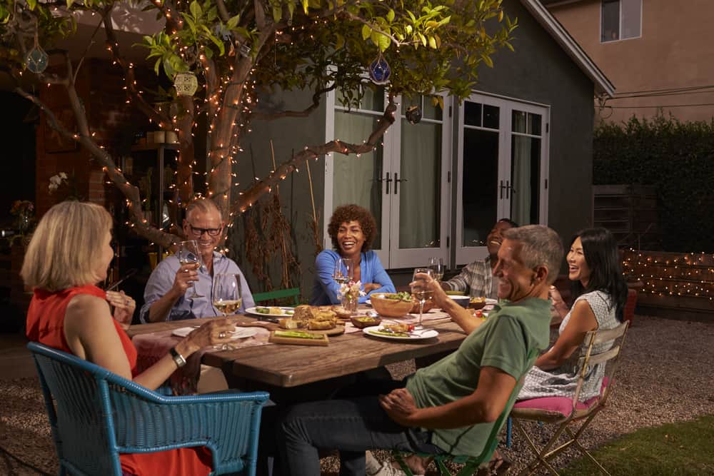Friends at an outdoor dinner party, smart lights in the background bringing ambiance.