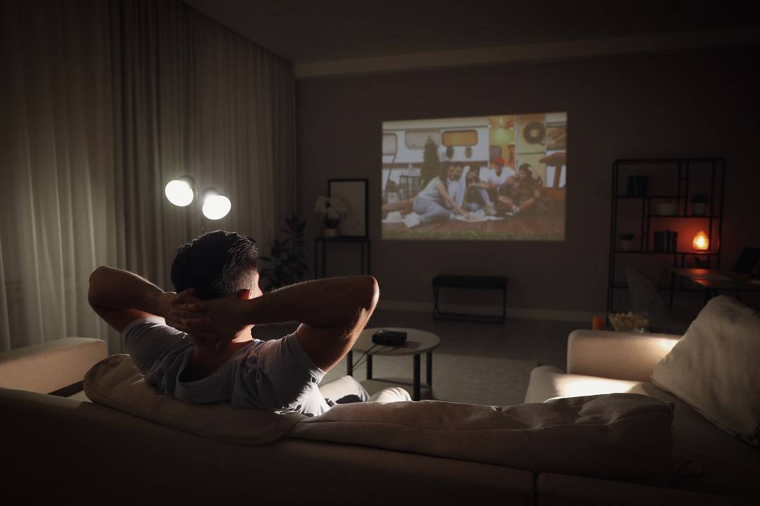 Man watching movie on sofa at night, back view.