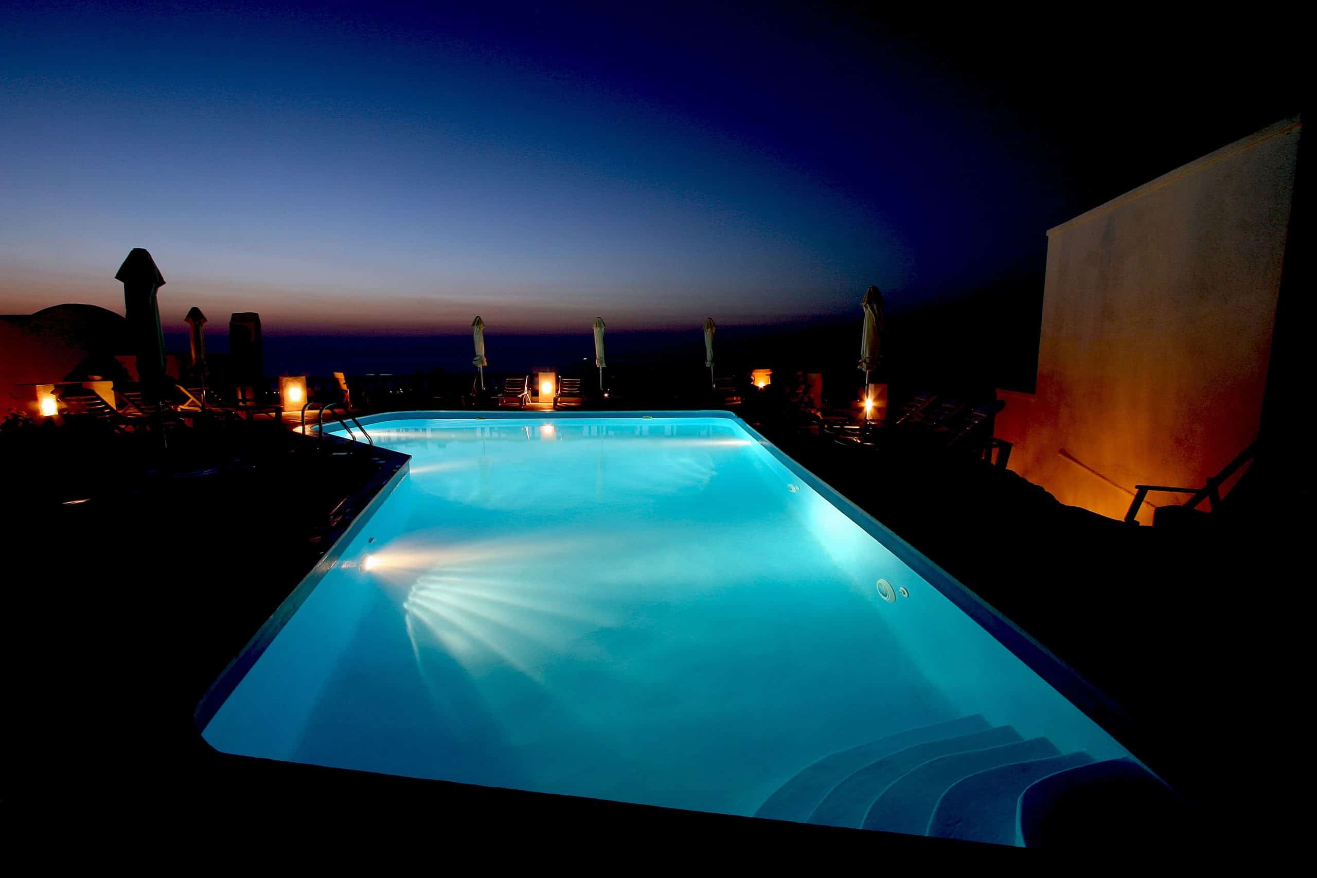 Swimming pool lit at night with faint sunset and ambiance lights.