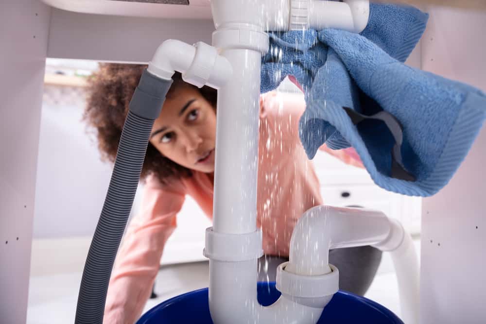 Woman looking at a water leak under sink, holding blue towel.