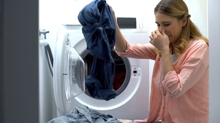 Woman closing nose from stinky clothes after washing