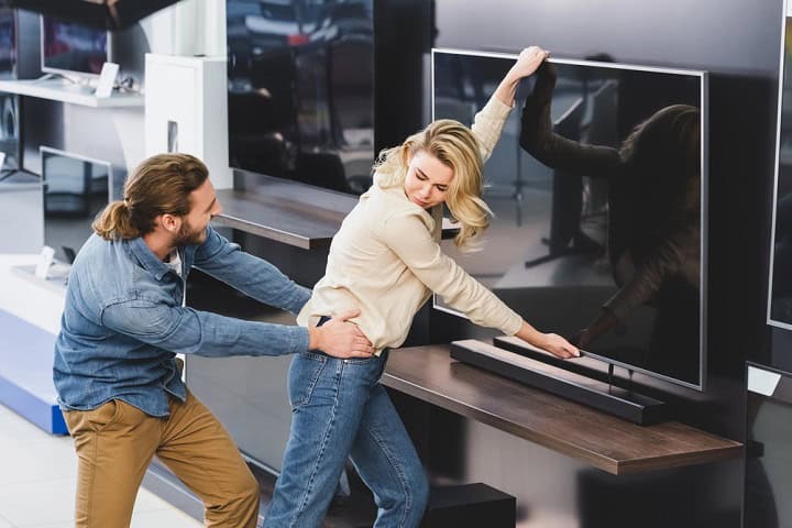 Angry boyfriend pulling girlfriend with tv in home appliance store