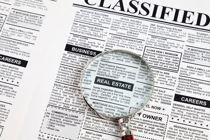 Classified ads in a newspaper with a magnifying glass sitting on a real estate ad.