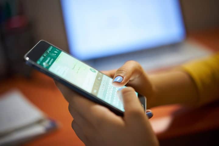 Woman using a messaging app on a cell phone, blurred out laptop in background.