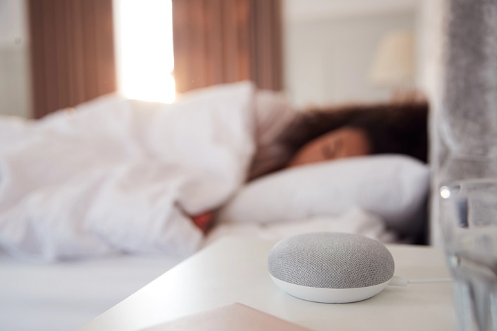 Woman sleeping in bed with voice assistant on bedside table.