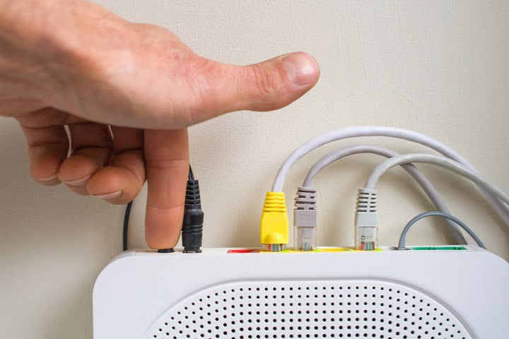 Person pushing a button on the back of a router.