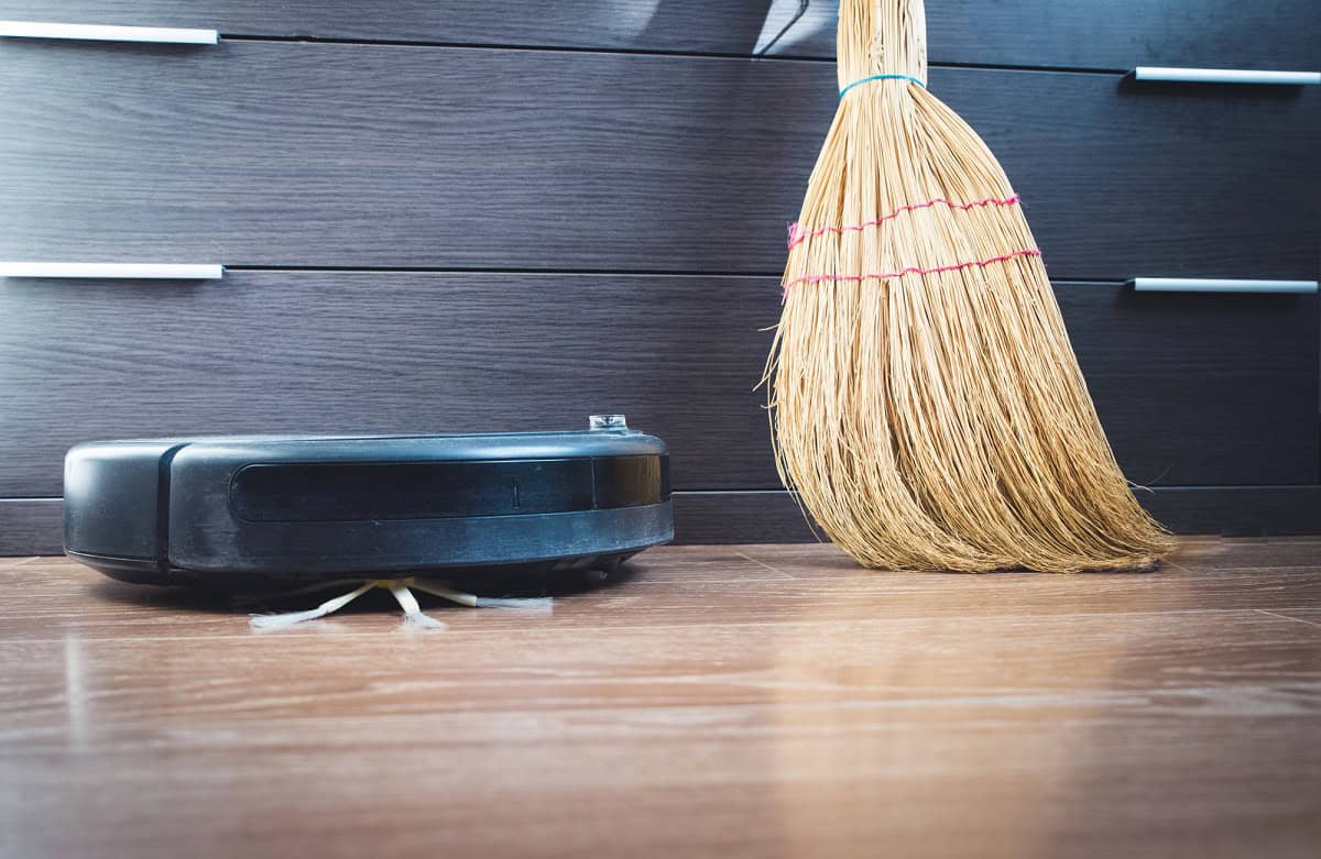 Robot vacuum and broom side by side.