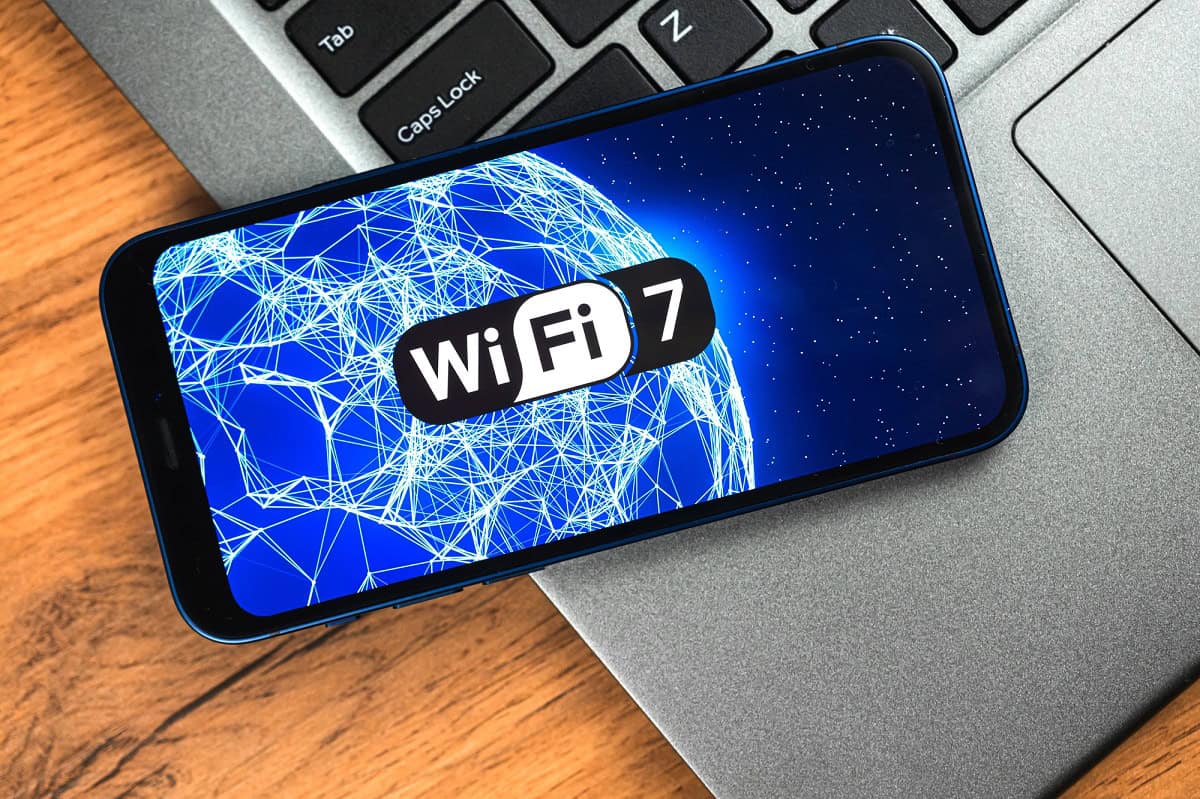 Cell phone with and image of a networked planet and Wifi7 logo. Cell phone is sitting on an open laptop keyboard.