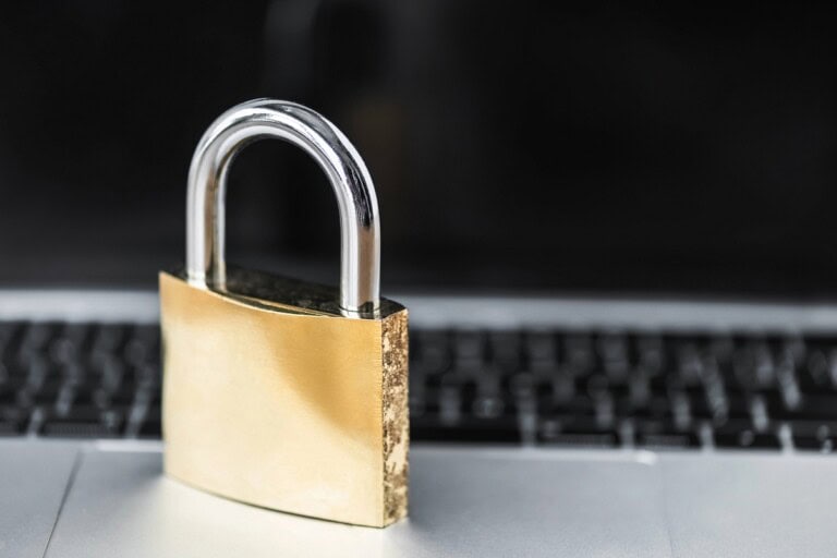 Padlock sitting on a laptop, keyboard and monitor in the background.