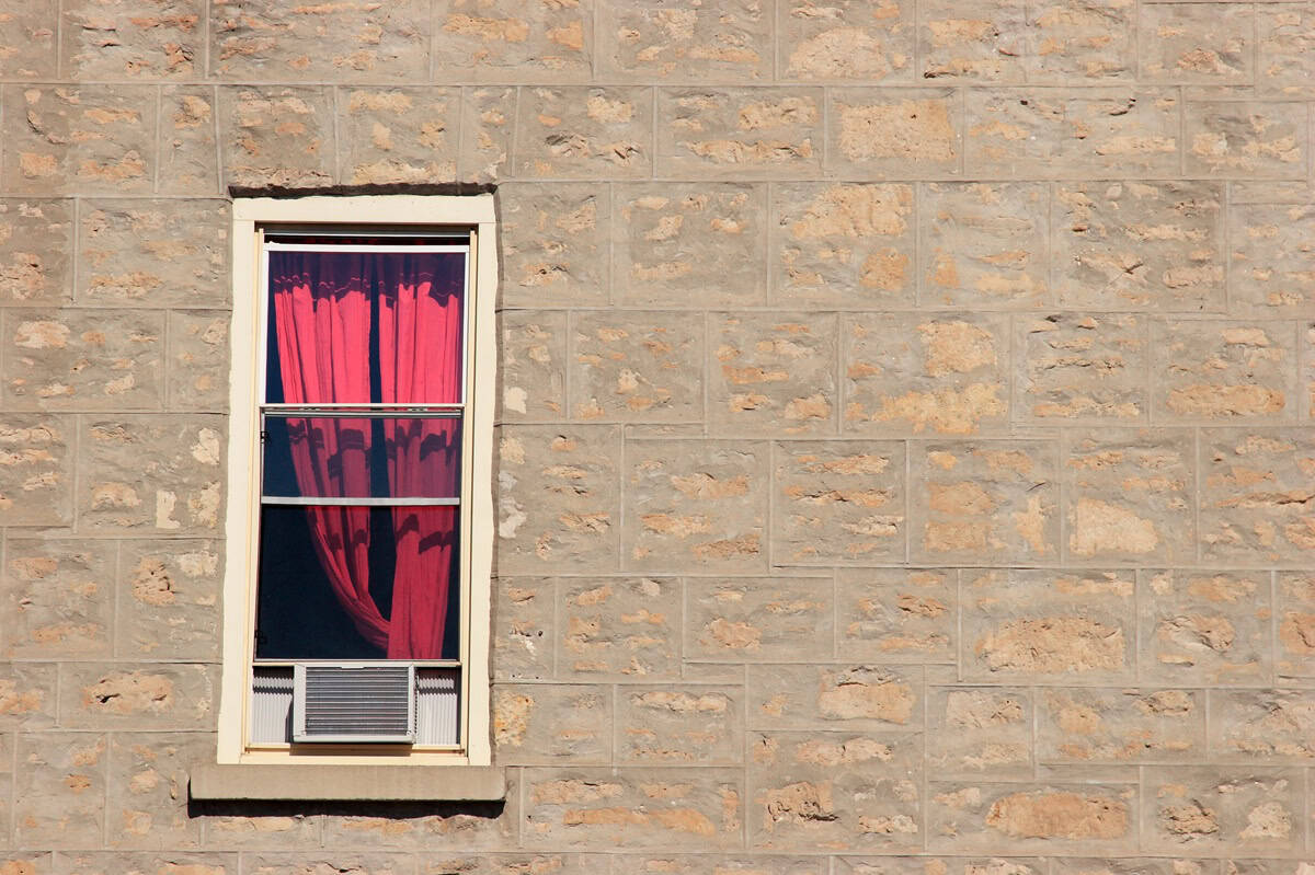 Window AC with red curtains in a brick building.