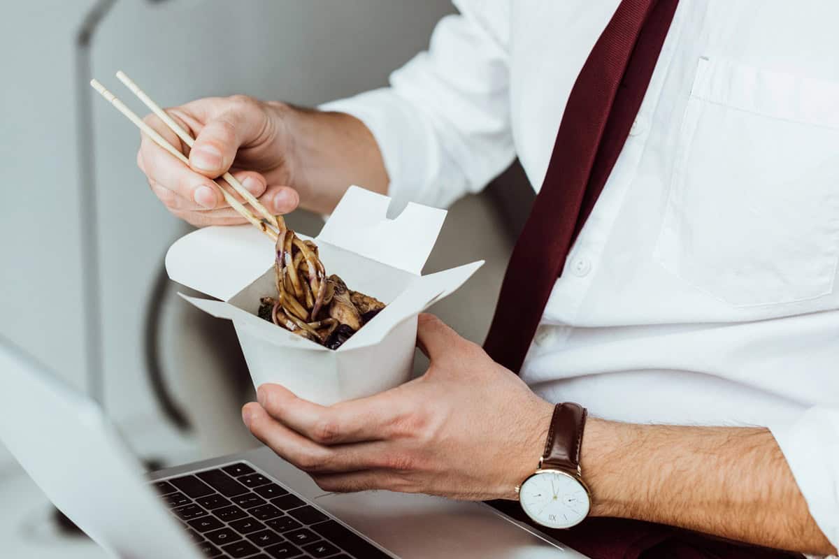 Cropped view of businessman with laptop eating noodles in office